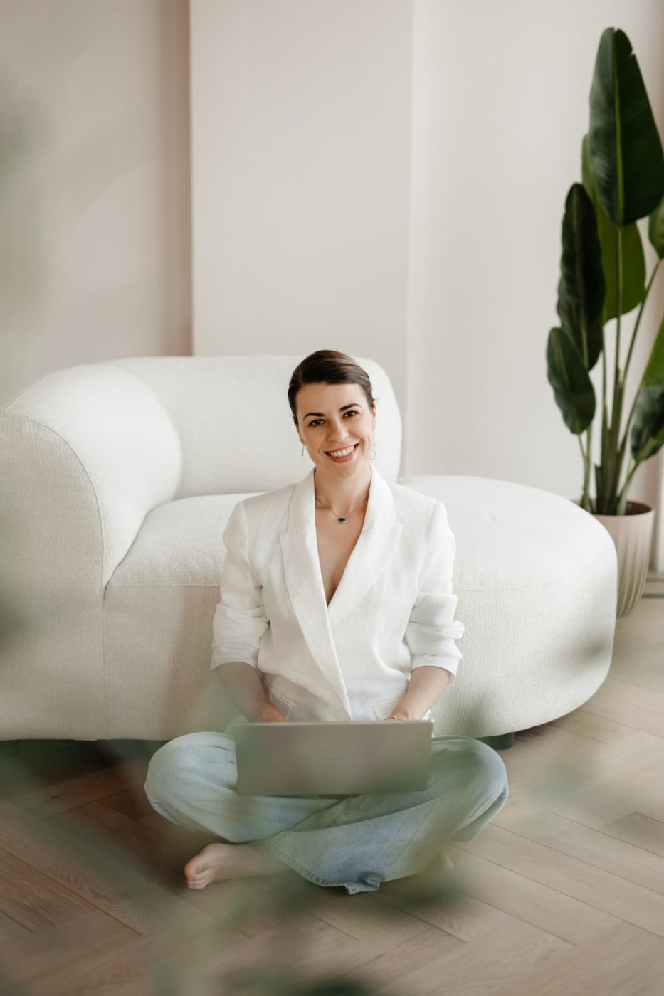 Alexandra sitting with her laptop beside a white sofa